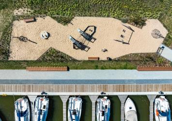 Widok na plac zabaw i nadbrzeże cumownicze z lotu ptaka. Widać plac zabaw i łodzie jachtowe zacumowane w porcie. 